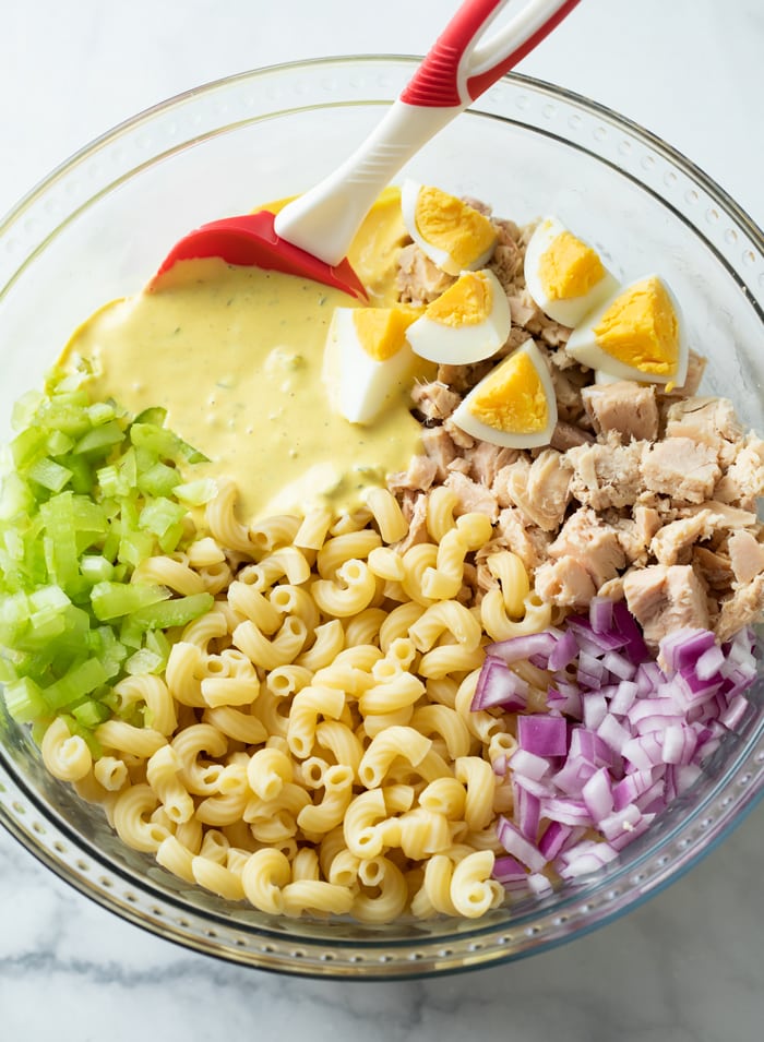Un bol en verre avec des ingrédients pour faire une salade de pâtes au thon avant d'être agité.