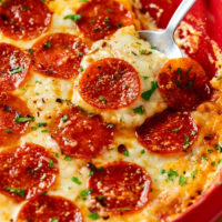 Une cuillère contenant une trempette à pizza chaude garnie de fromage fondu et de pepperoni.