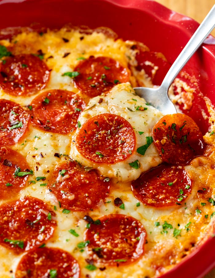 Une cuillère ramassant une trempette à pizza au fromage avec du fromage mozzarella et du pepperoni.
